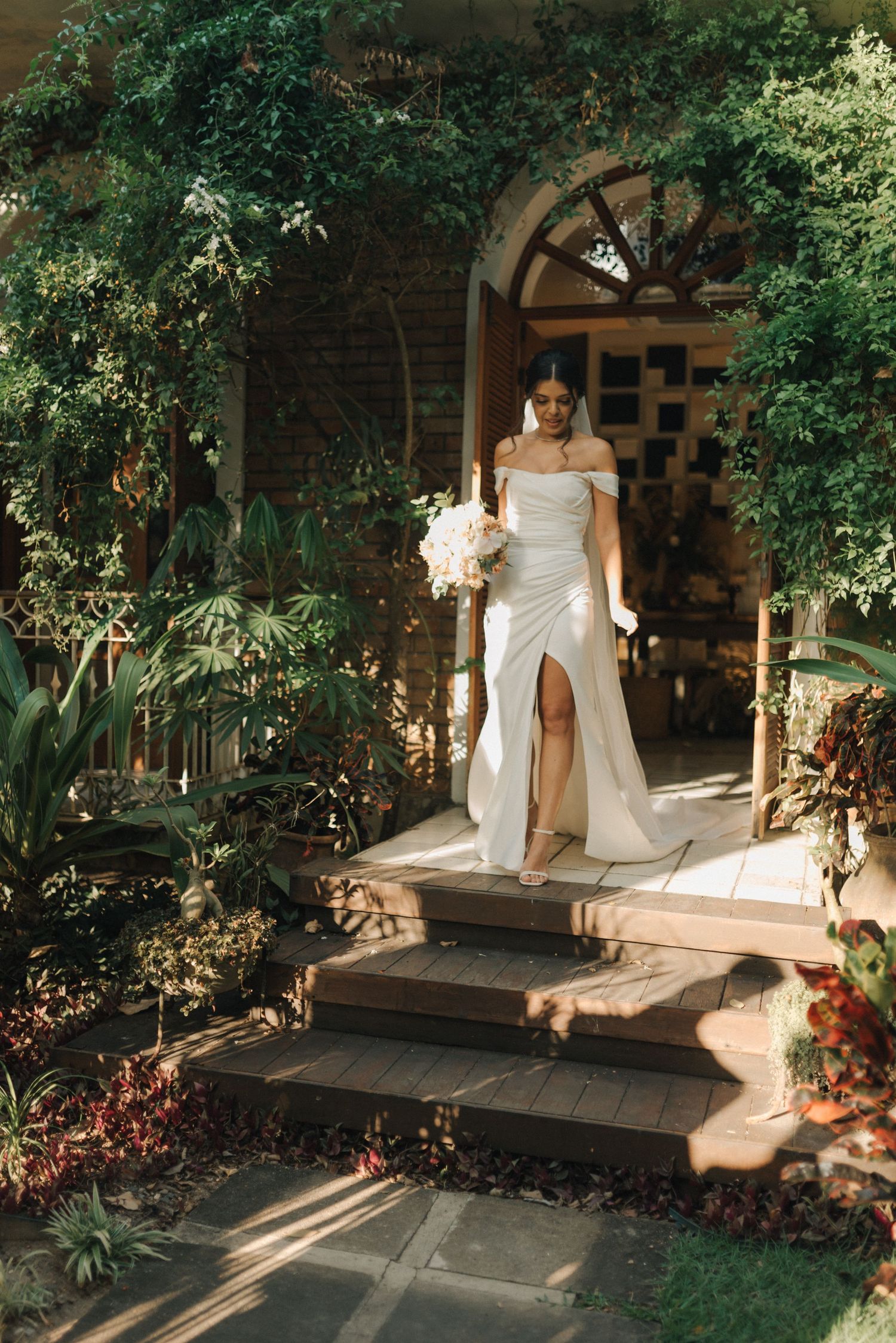 Elegant wedding dress captured in natural light on garden steps framed by lush greenery.