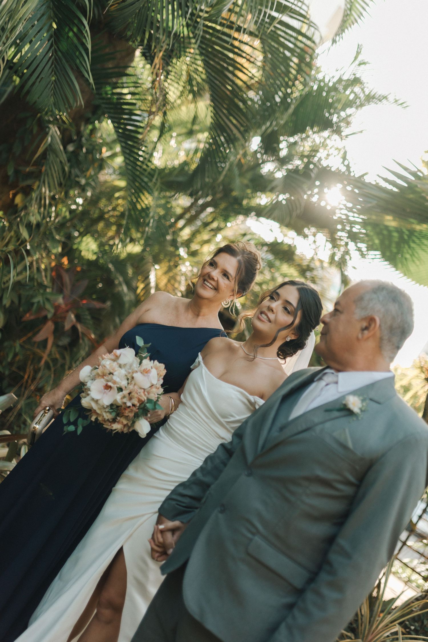 Wedding party poses in tropical garden setting with palm trees and natural sunlight.