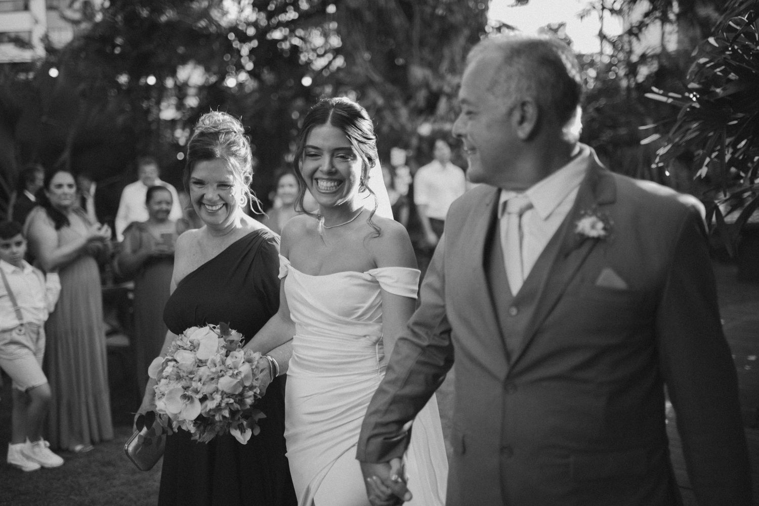 Black and white capture of wedding party walking together outdoors with guests in background.