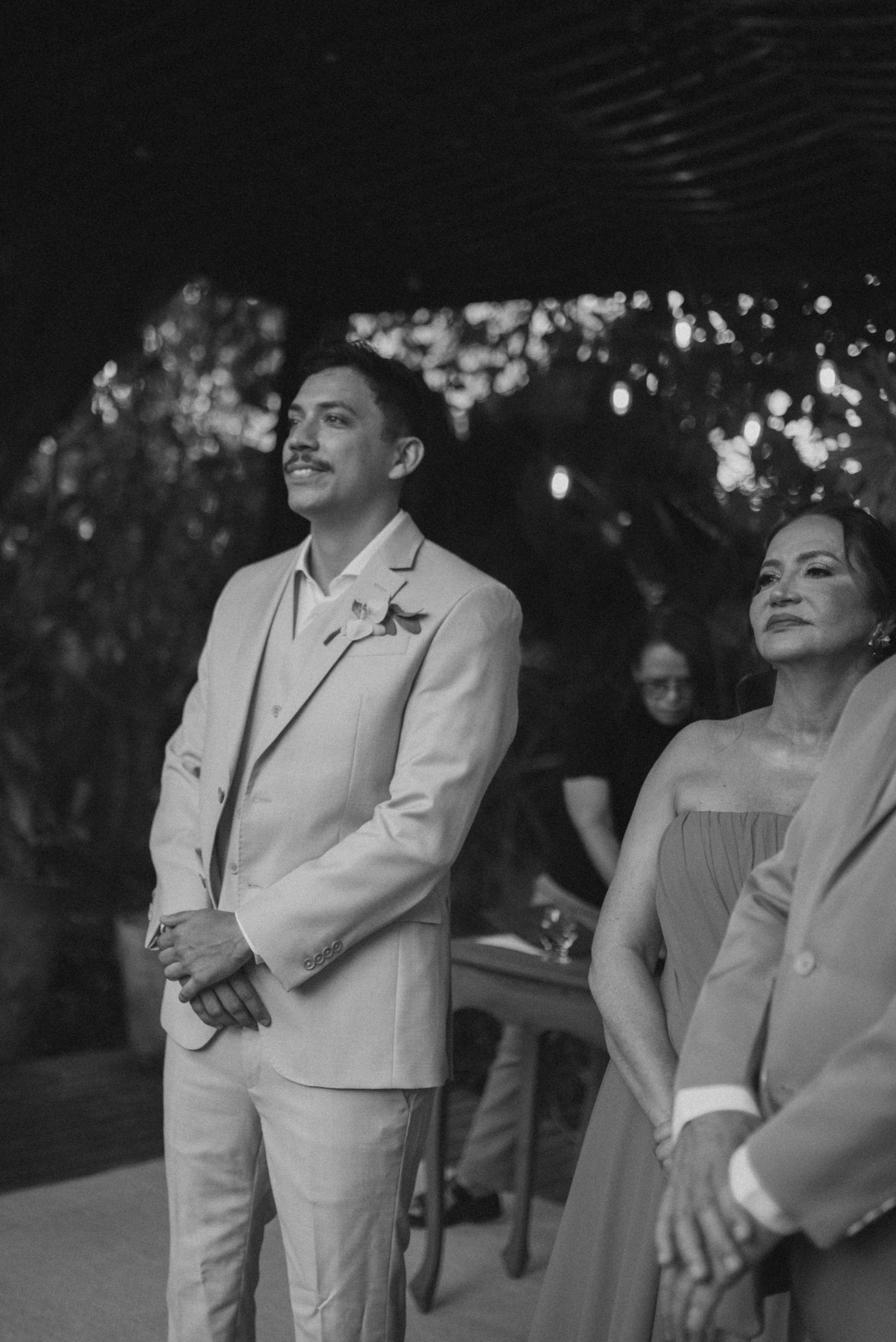 Black and white photo of formal event attendees watching ceremony in outdoor garden setting.