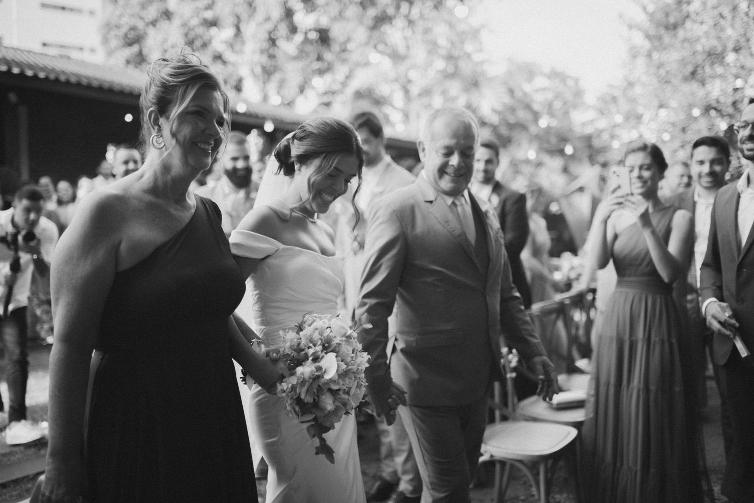 Wedding couple embracing with guests during outdoor celebration in black and white photography.
