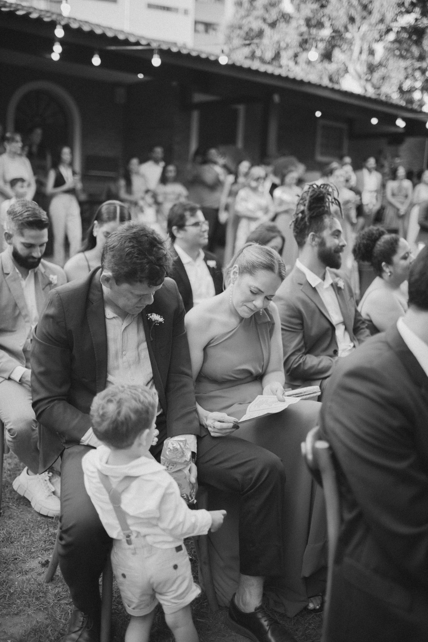 Black and white photo of wedding guests interacting with small child in formal attire.