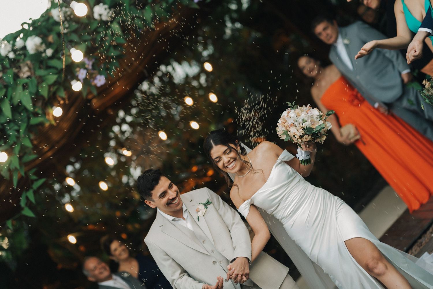 Wedding couple celebrates during outdoor reception under string lights and greenery.