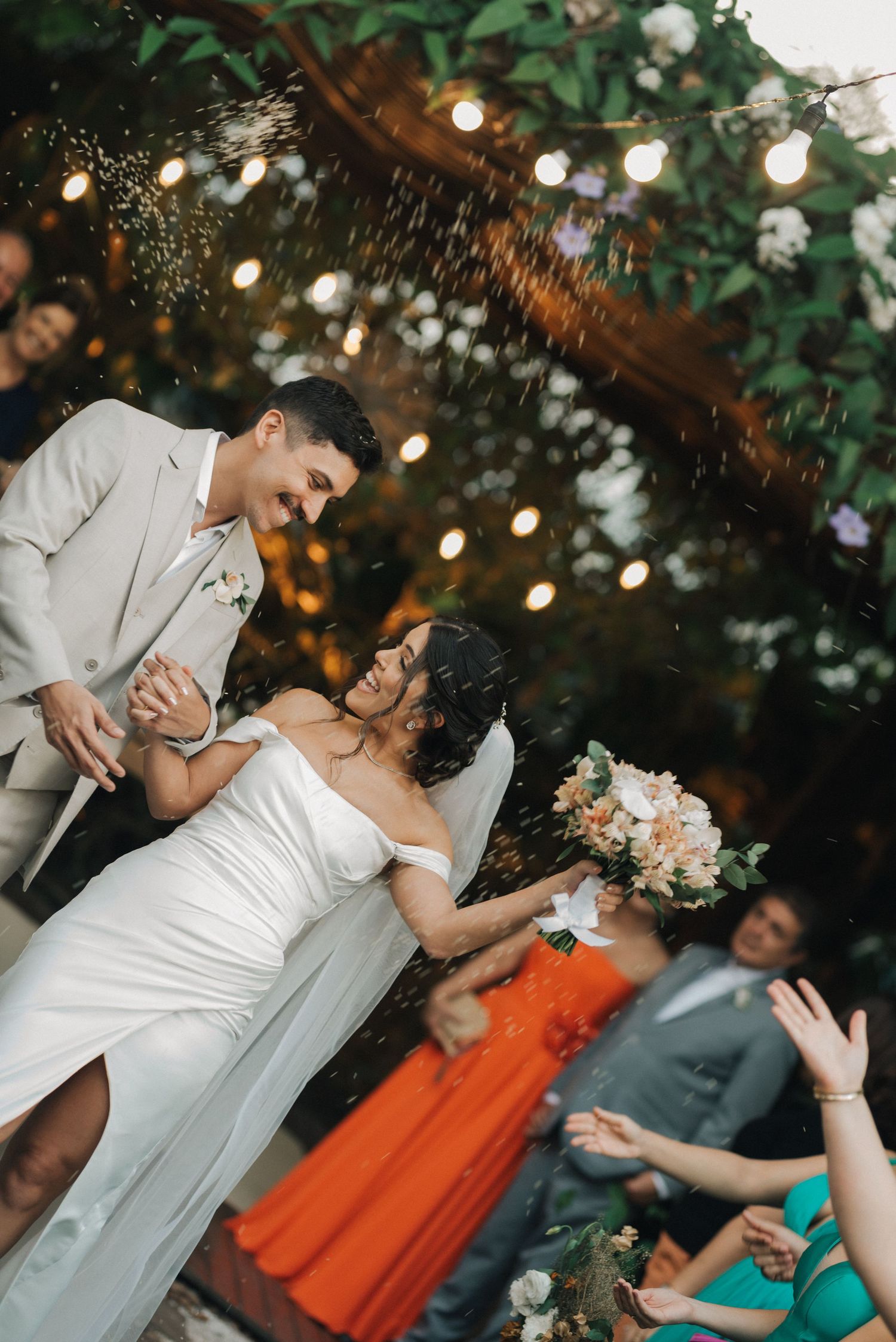 Newlyweds celebrate with champagne under string lights and floral decorations.