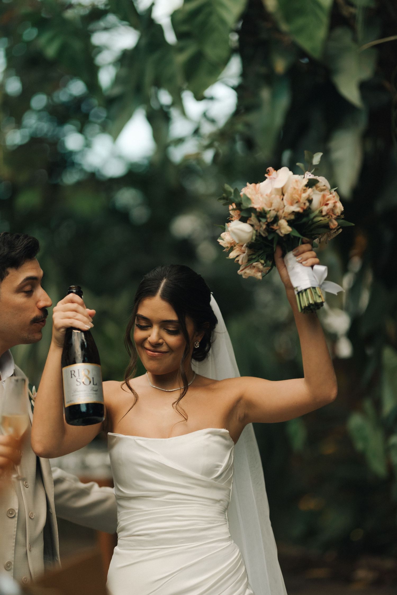 Newlyweds celebrate with champagne and a bouquet in a lush garden setting.