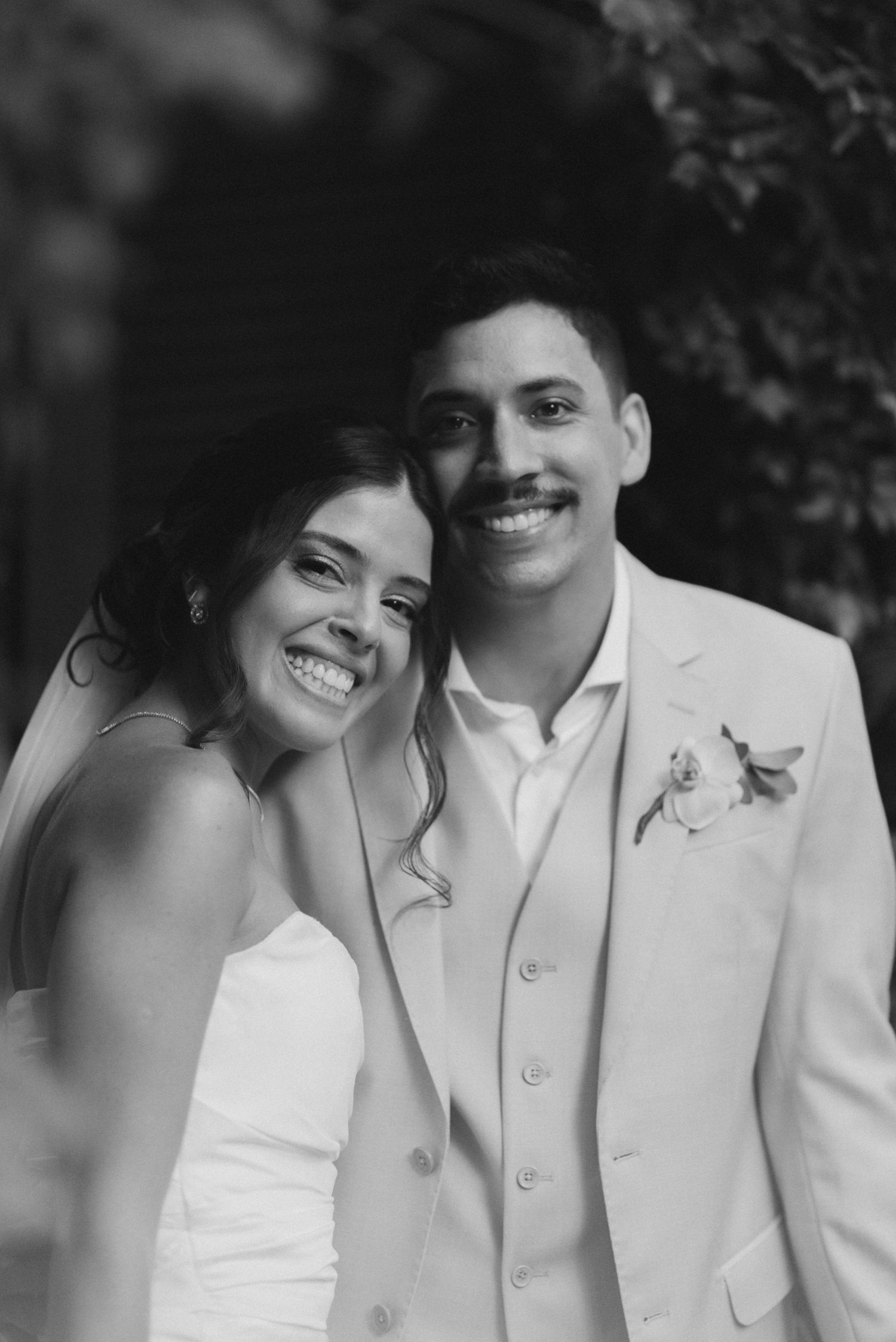 A joyful wedding couple shares an intimate black and white portrait outdoors.