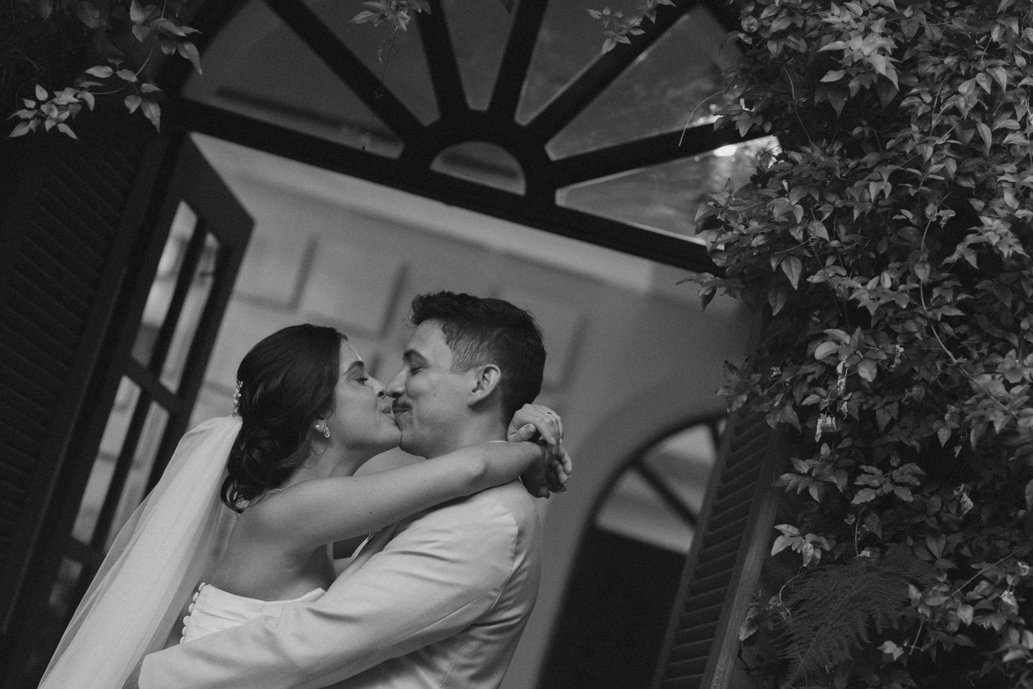 Black and white romantic embrace between newlyweds under an arched doorway.