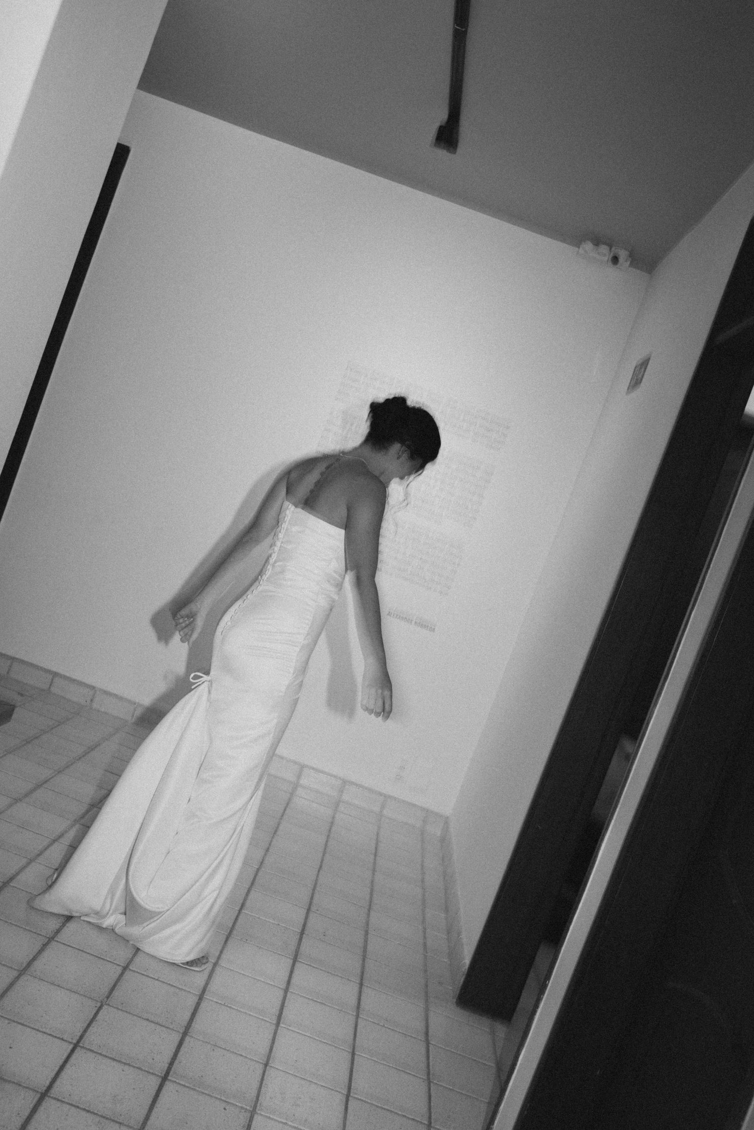 Artistic black and white shot of bride in sleek wedding dress walking down hallway.