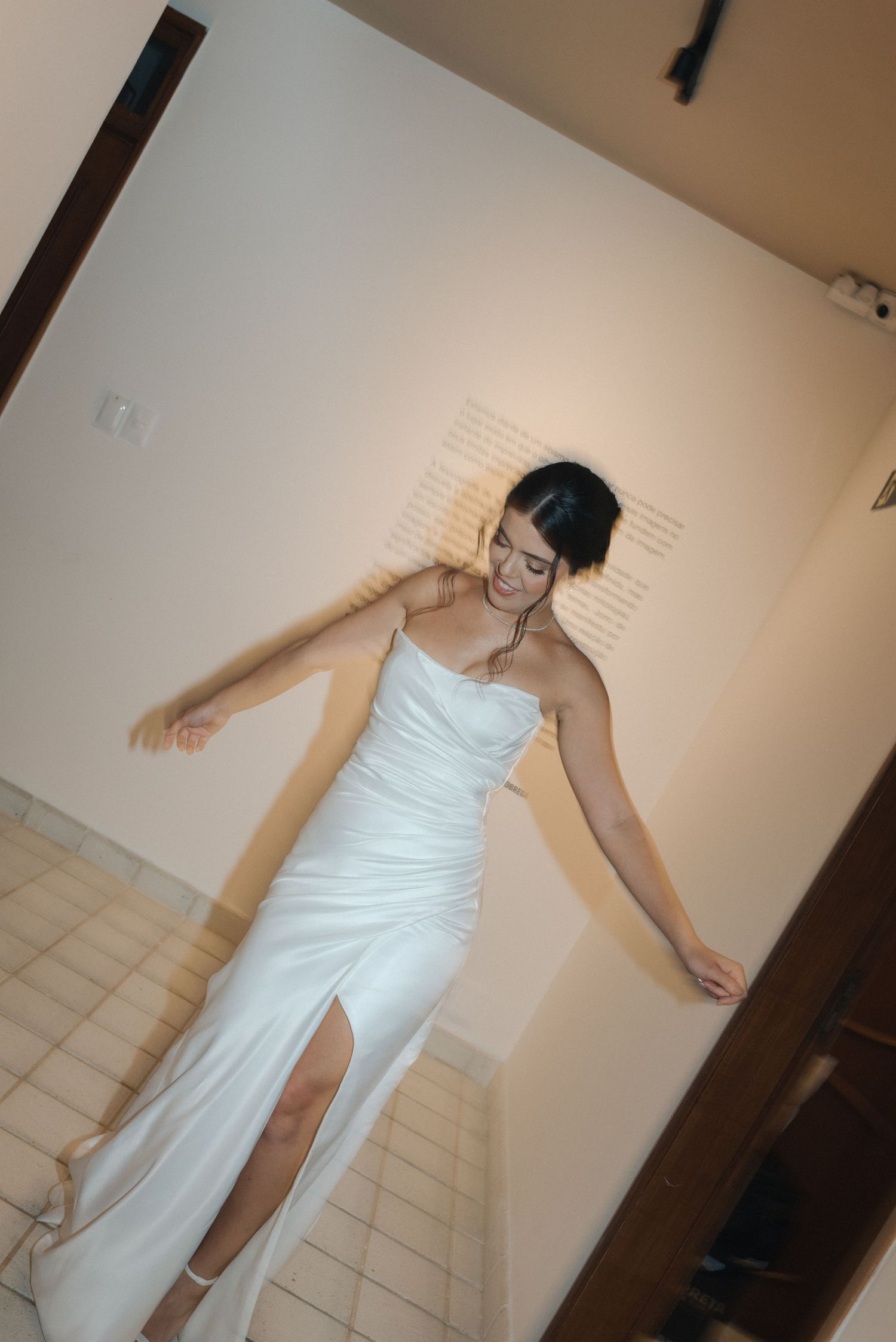 A person dances gracefully in a fitted white wedding dress against a neutral wall background.