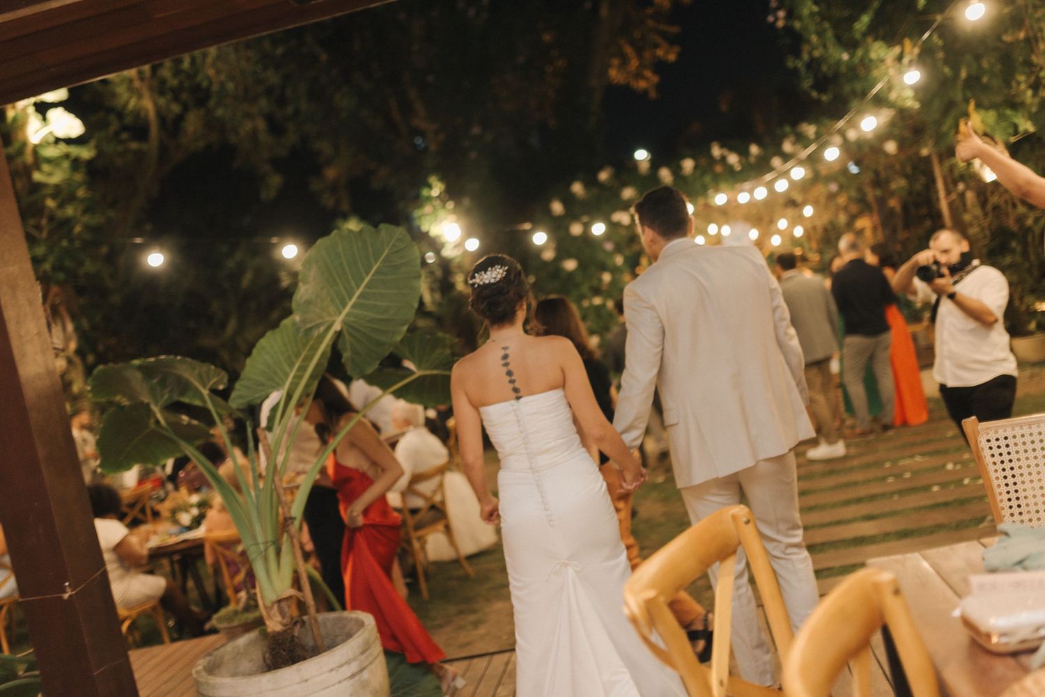An outdoor wedding reception with string lights and tropical plants creating a romantic atmosphere.