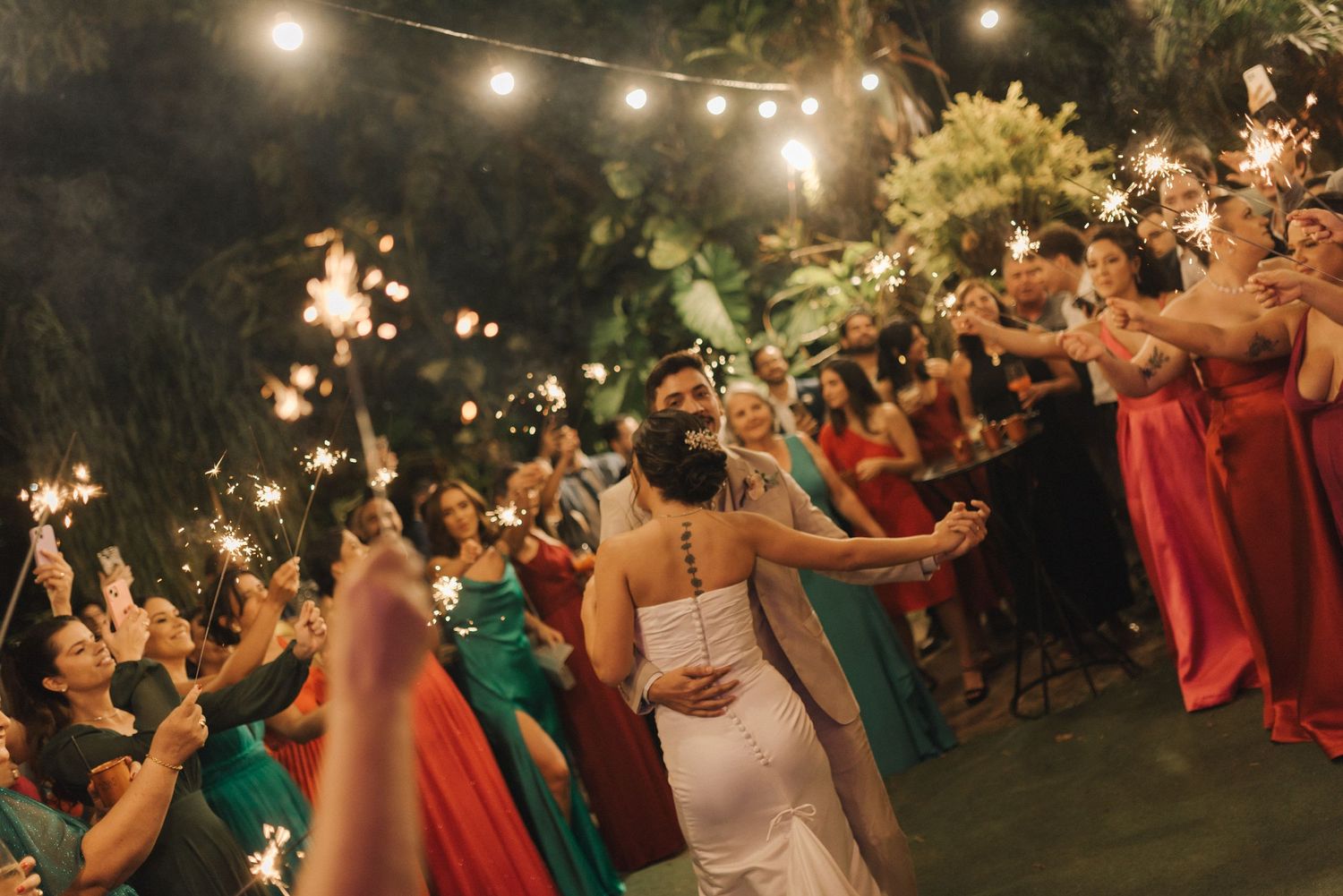 Wedding celebration under string lights with guests in colorful attire joining the festivities.