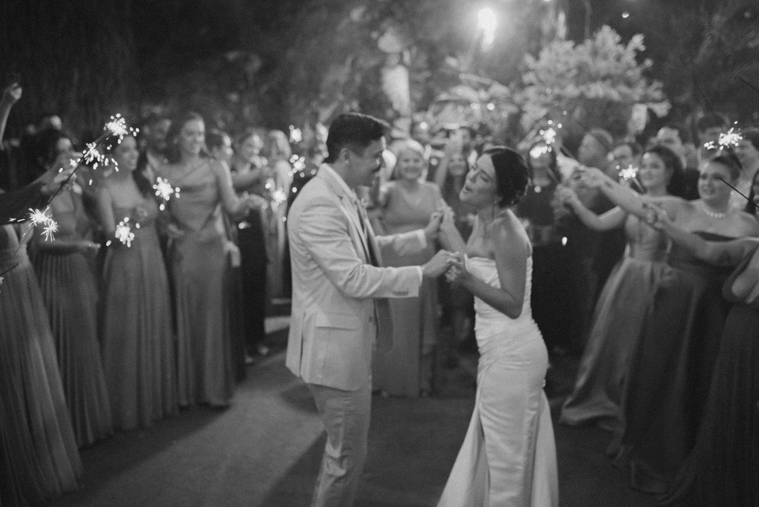 A couple shares their first dance surrounded by guests holding sparklers at night.