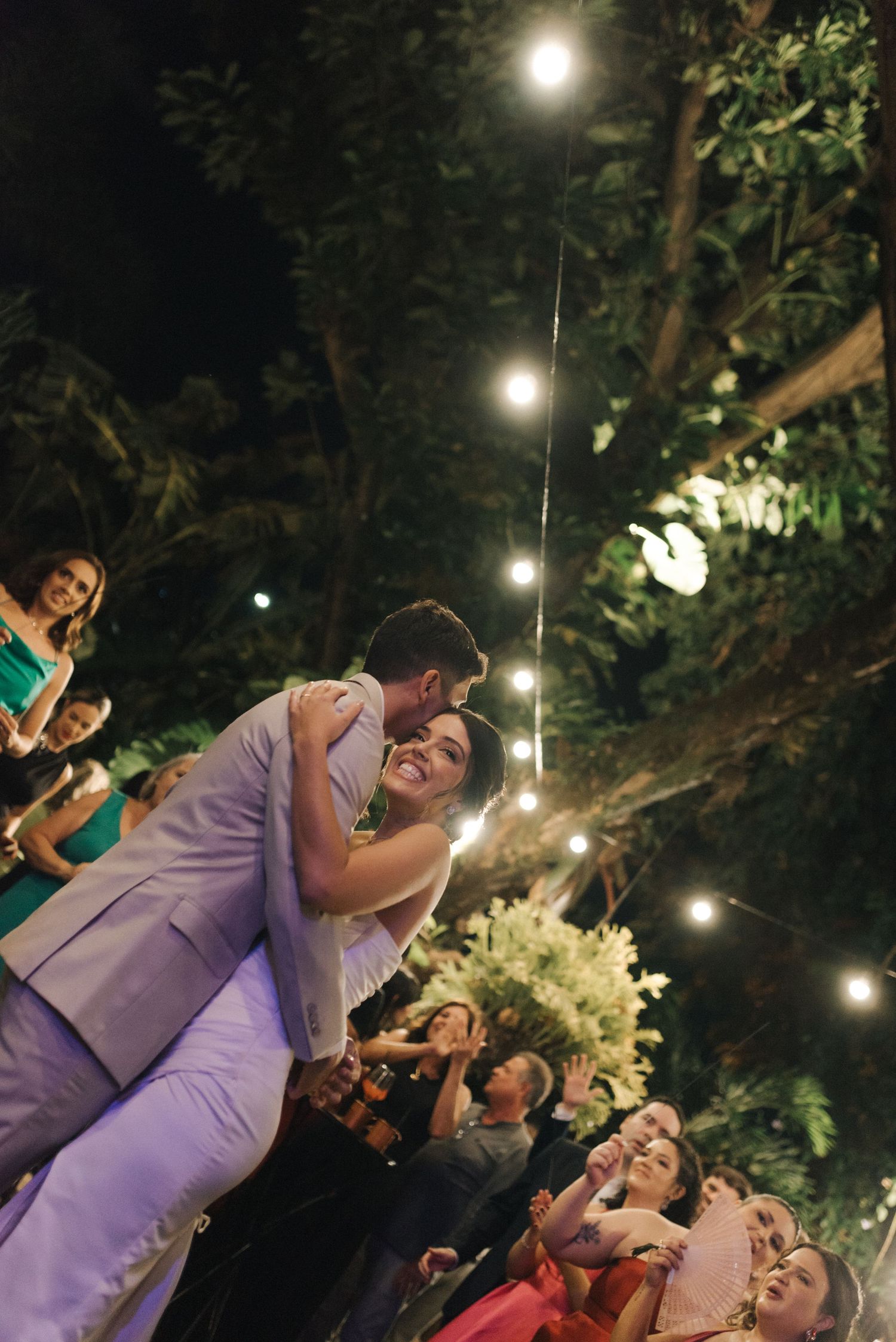 Wedding couple dancing beneath twinkling lights strung between trees at an outdoor reception.