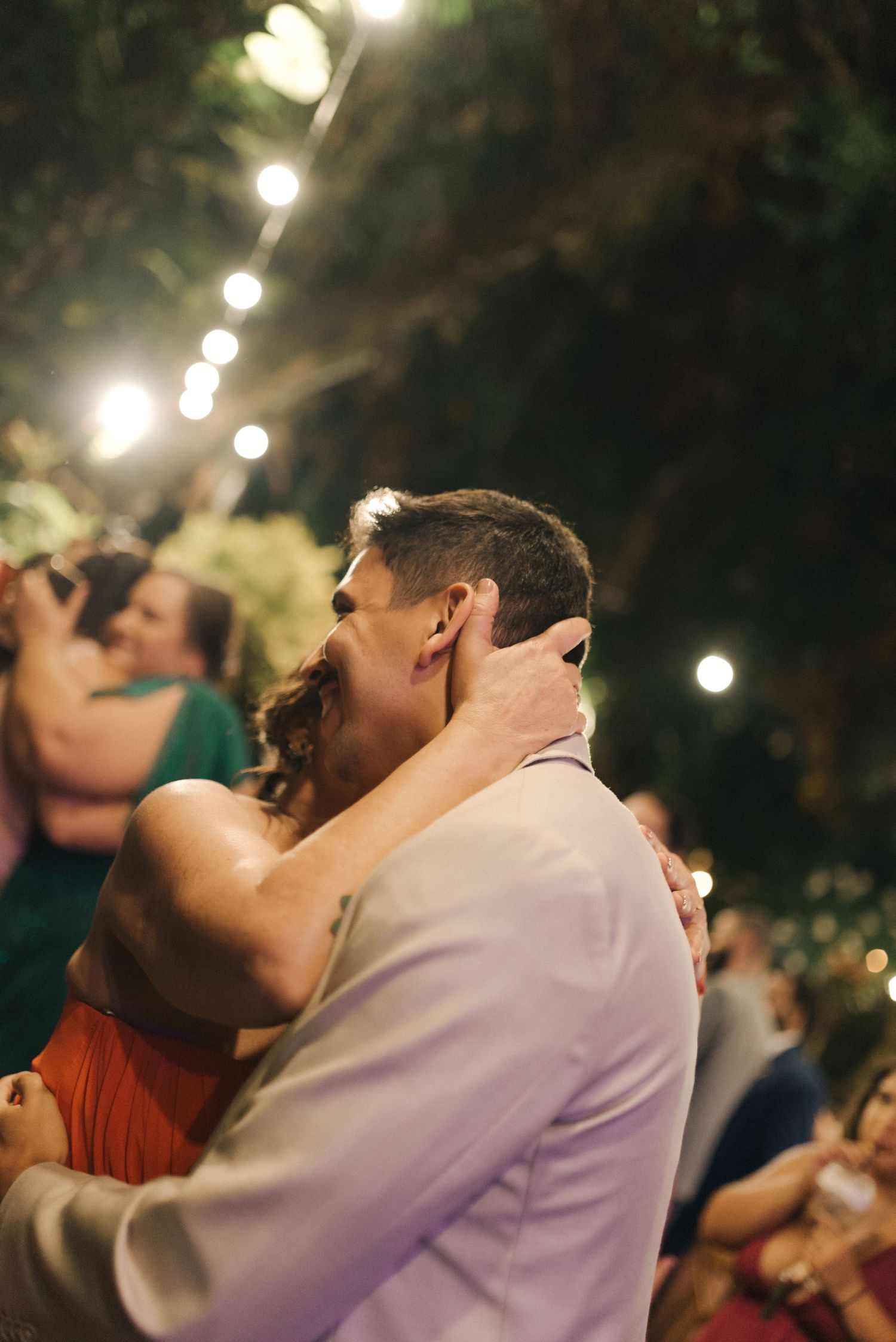 Dancing couple embraces during a romantic moment under string lights at an outdoor celebration.
