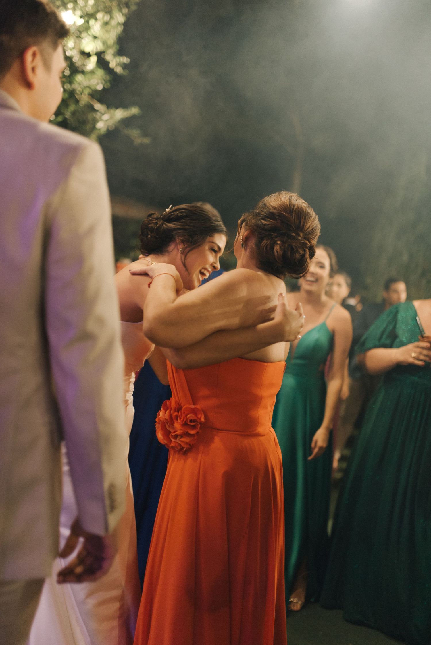 Wedding guests in formal attire dance and celebrate at an outdoor evening reception.