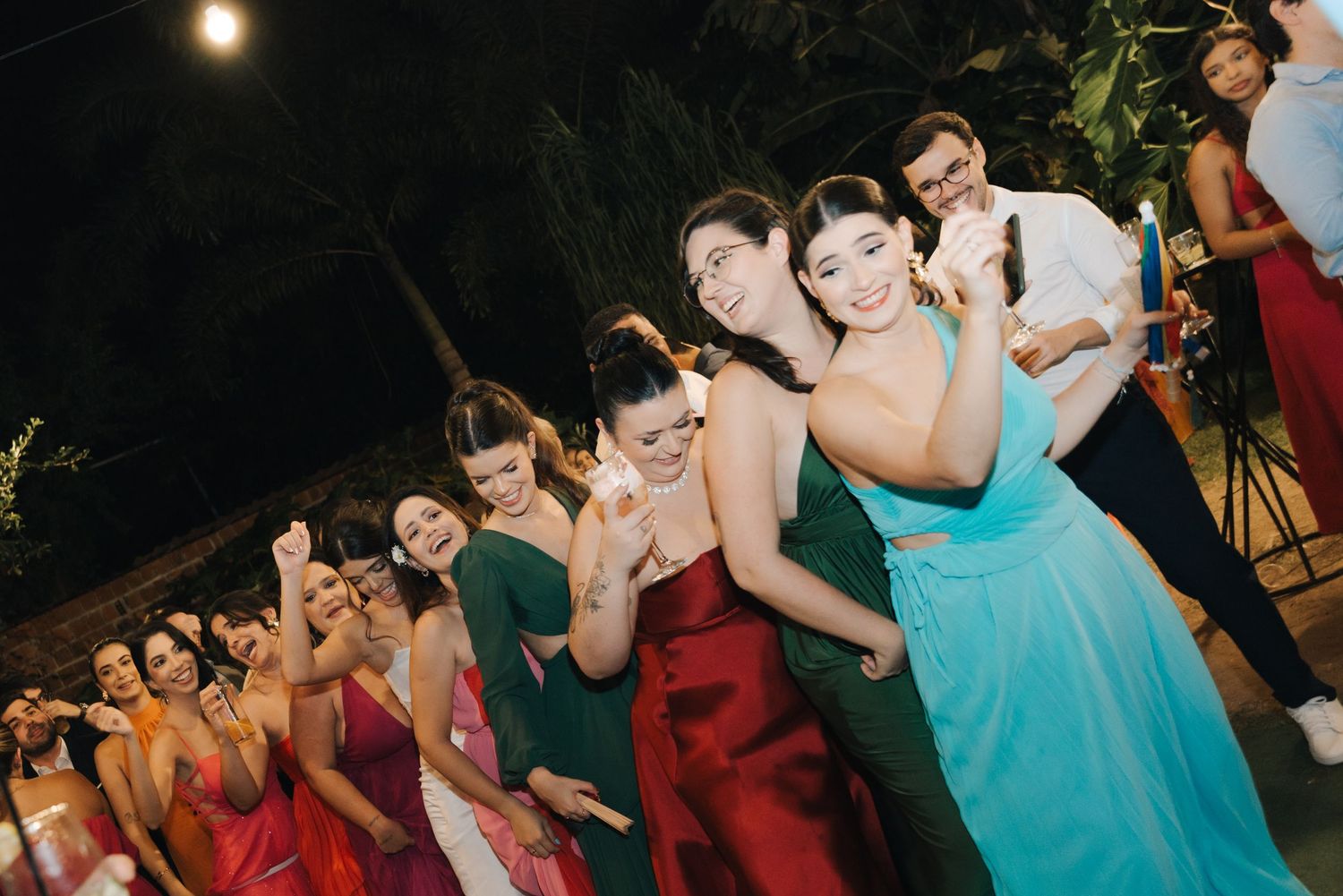 Wedding party in colorful dresses poses playfully at an outdoor evening reception.