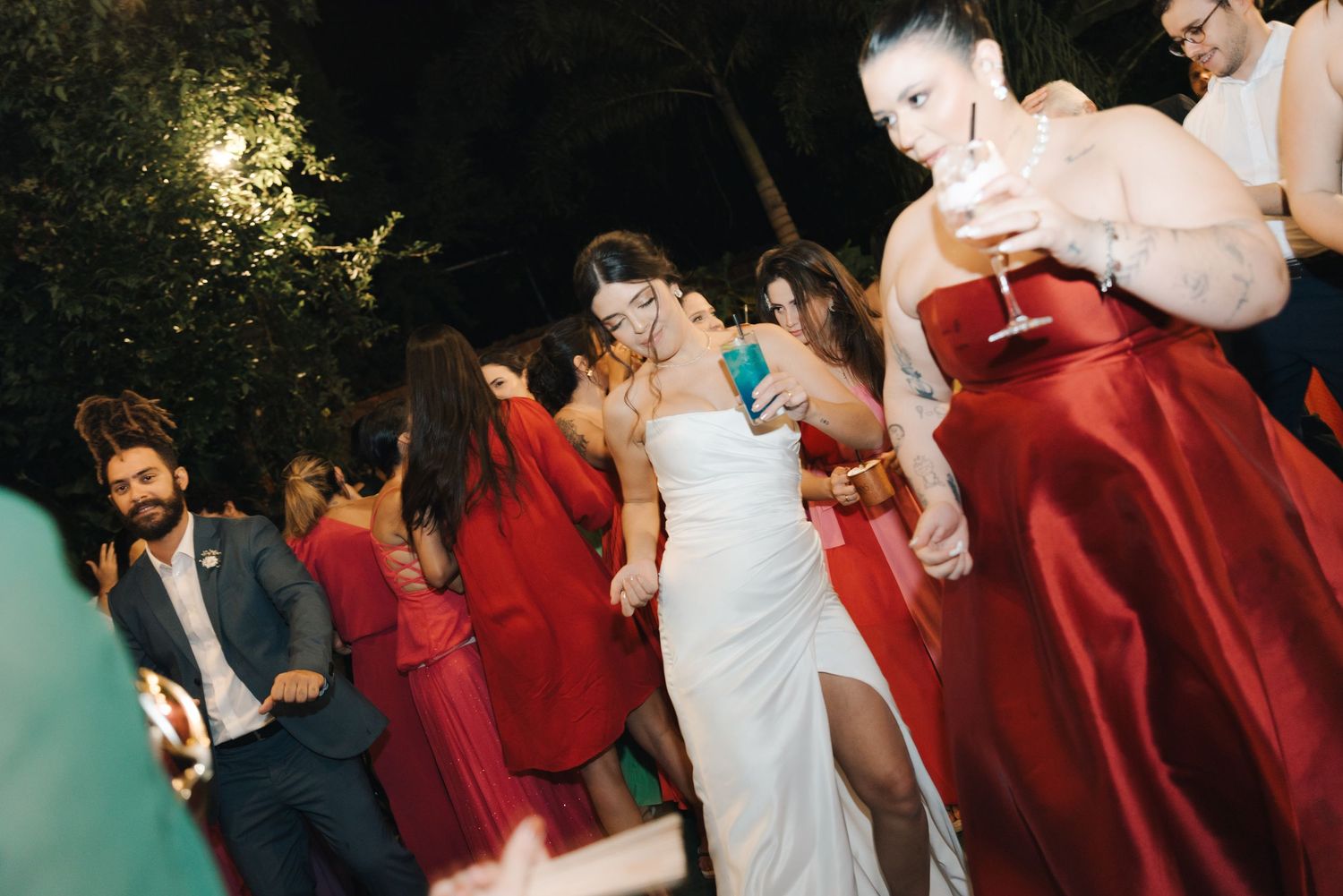 Wedding celebration with people dancing in red bridesmaid dresses and formal attire.