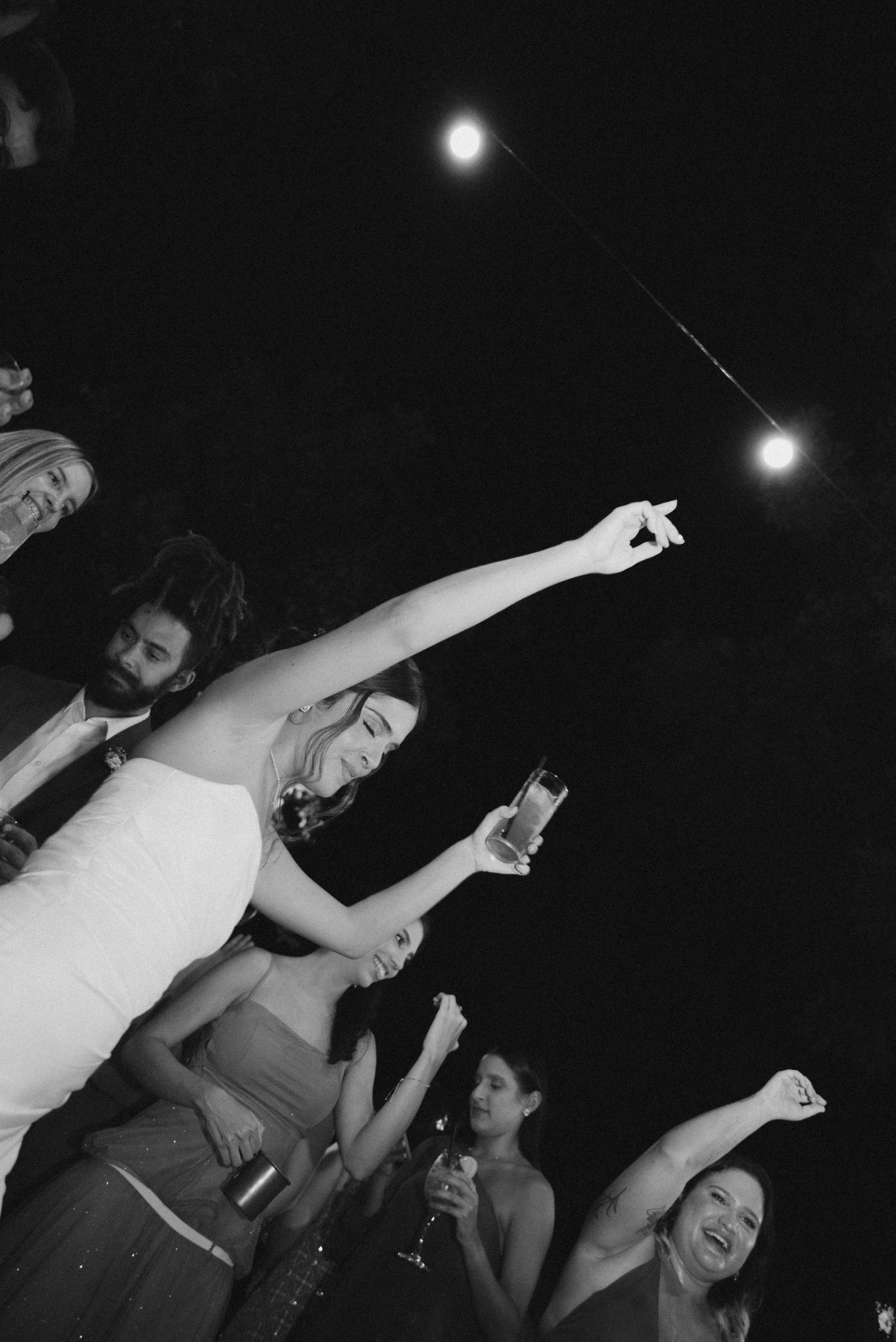 People dancing and celebrating under string lights at a night event.