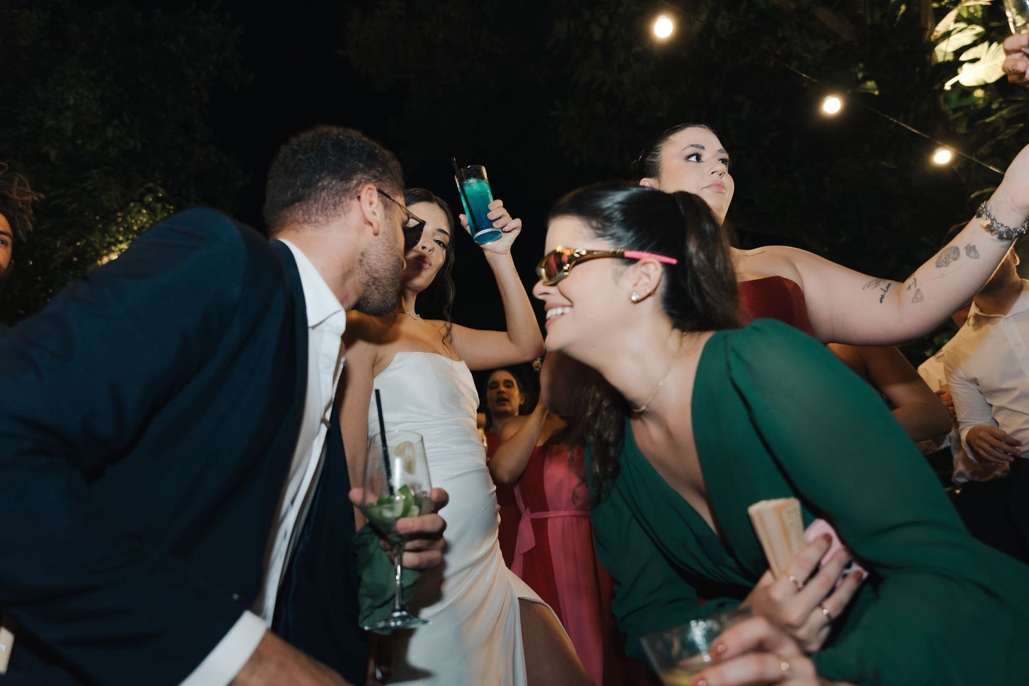 Partygoers dancing and laughing while holding drinks at an outdoor celebration.