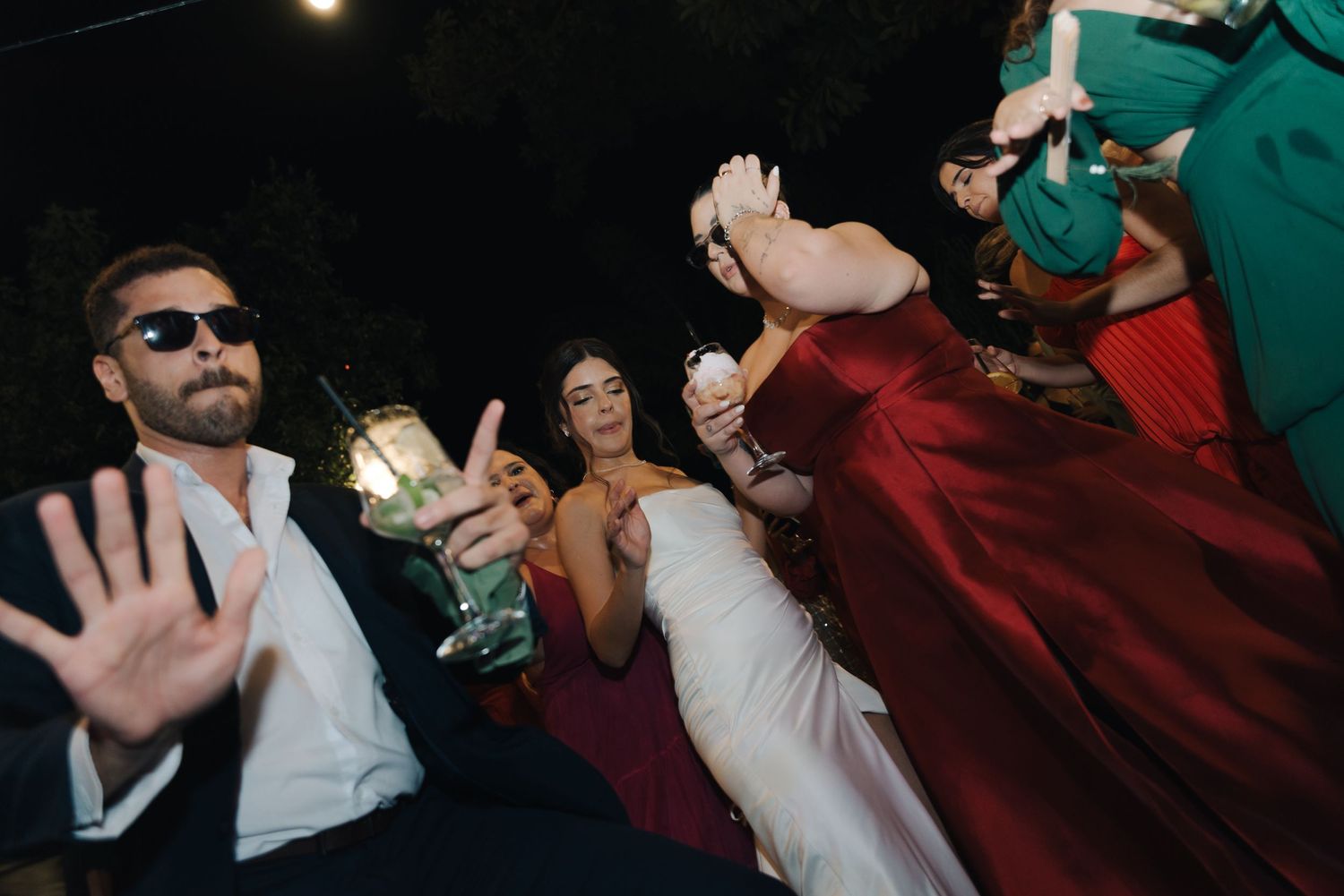 Energetic party scene with guests dancing and holding drinks under outdoor lighting.