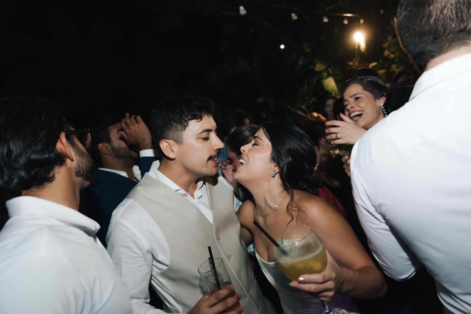 Wedding guests dancing and celebrating at a nighttime reception with drinks in hand.
