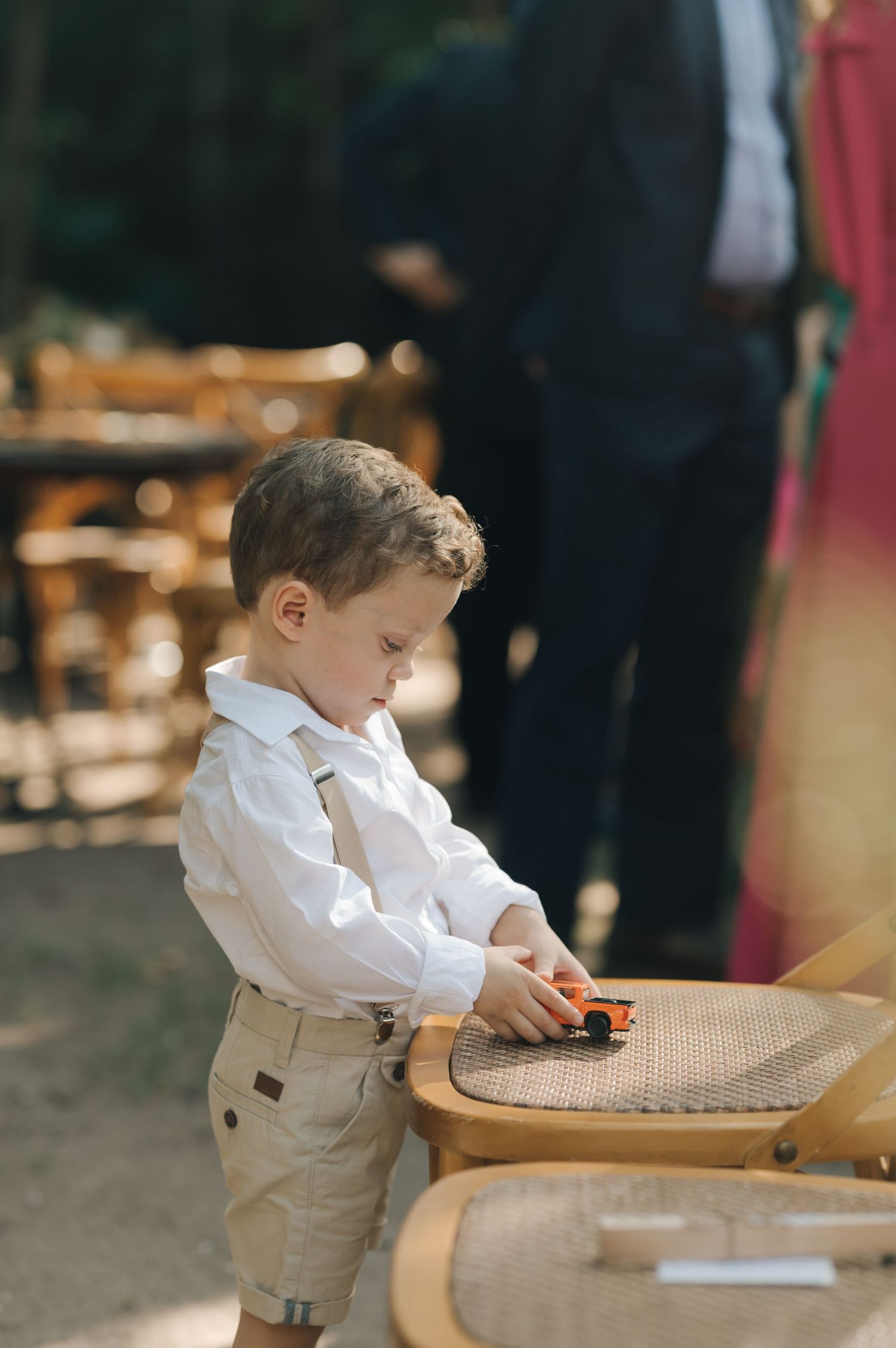 Small child in formal wear playing with toy car on outdoor furniture.