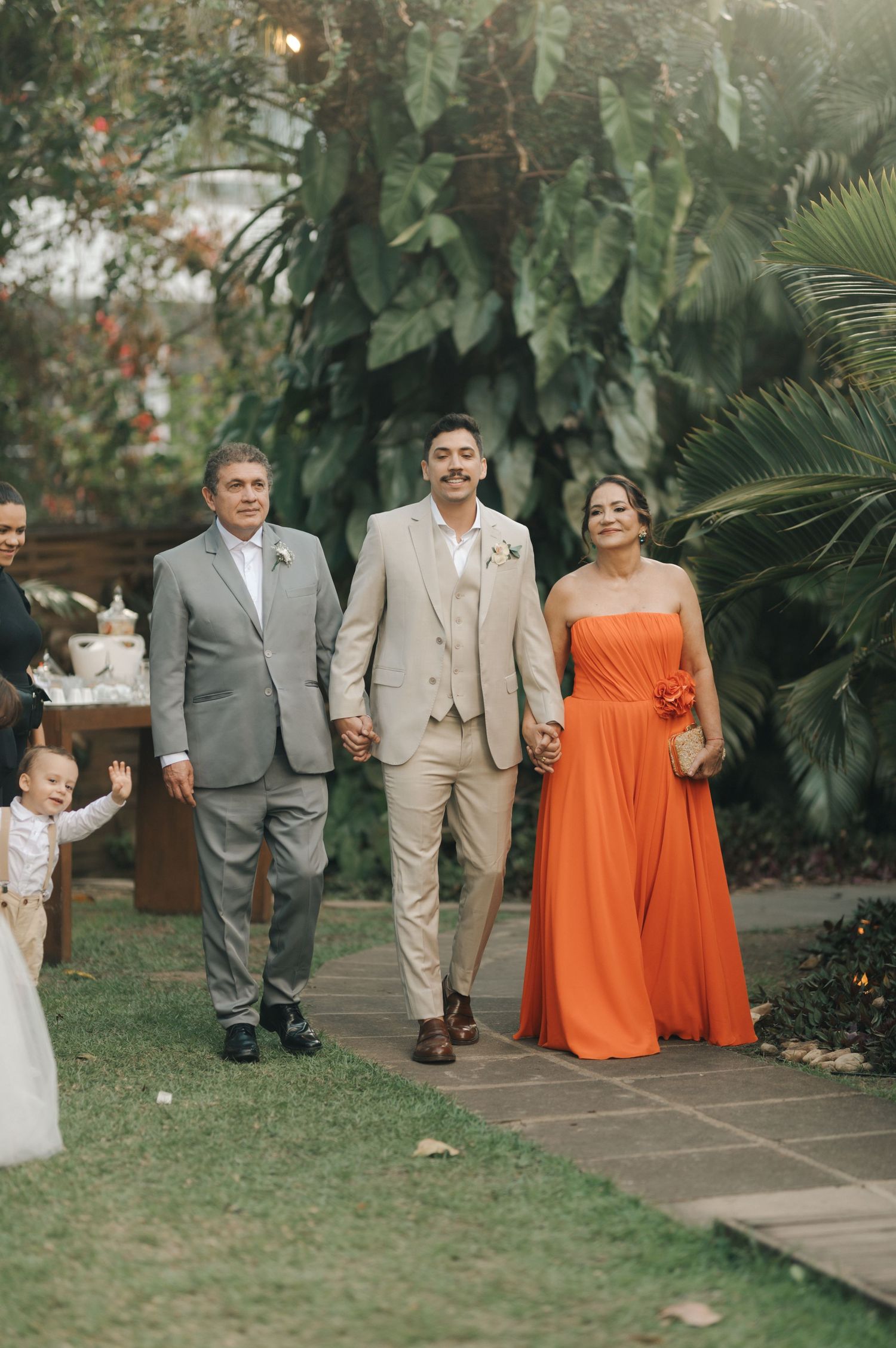 Wedding party walking down garden pathway with lush tropical foliage backdrop.