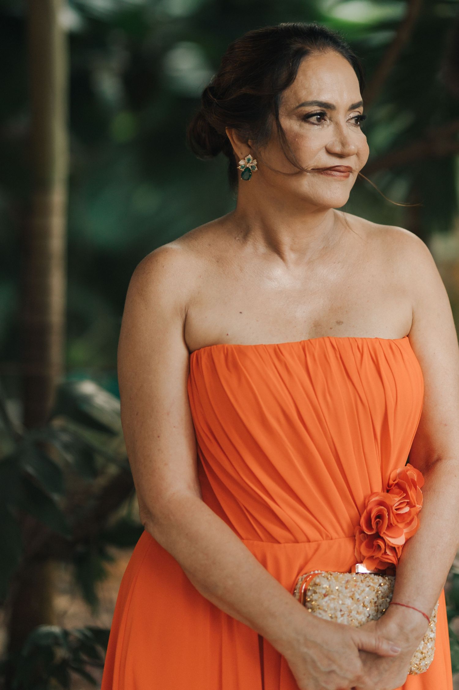 Woman in vibrant orange strapless gown with clutch purse at outdoor event.