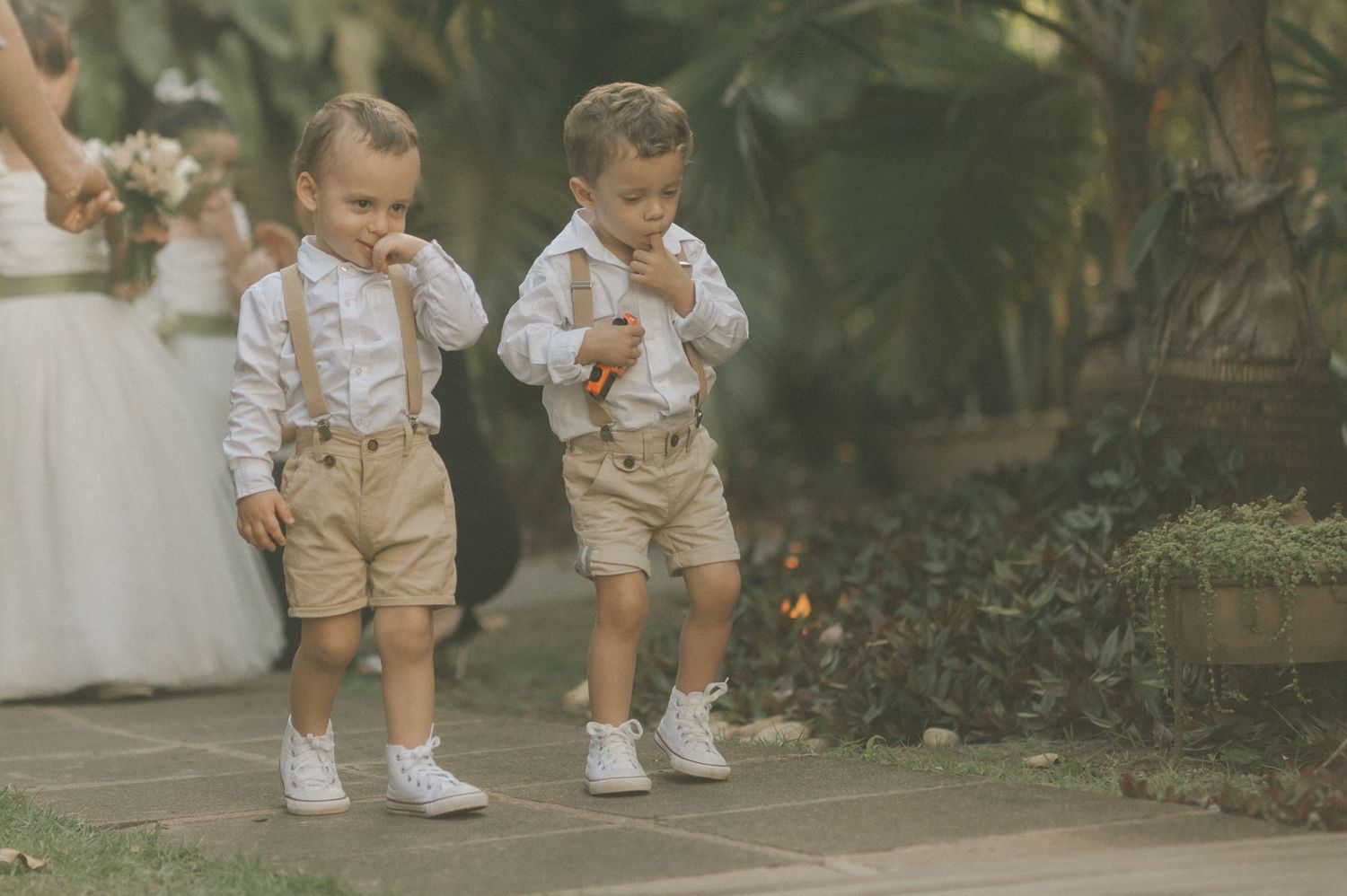 Two young children in matching formal outfits with suspenders at garden event.