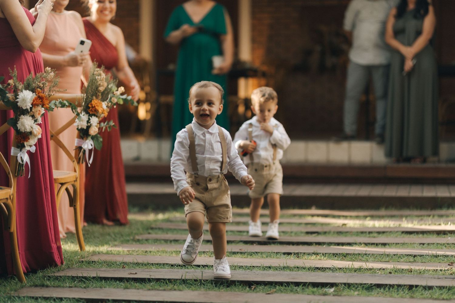 Two young ring bearers in formal attire running down steps at an outdoor wedding ceremony.