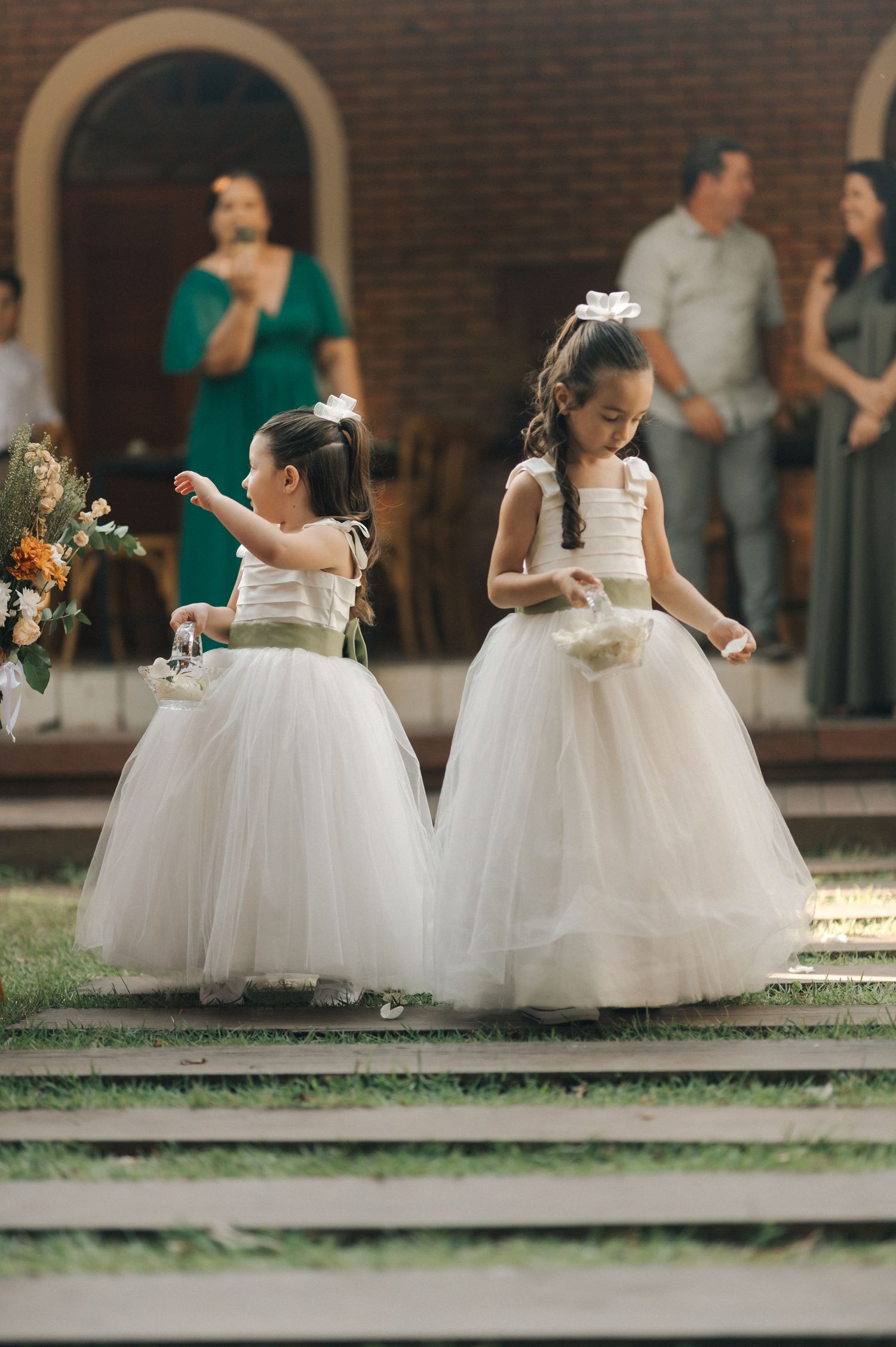 Two flower girls in white tulle dresses standing on outdoor steps during a wedding ceremony.