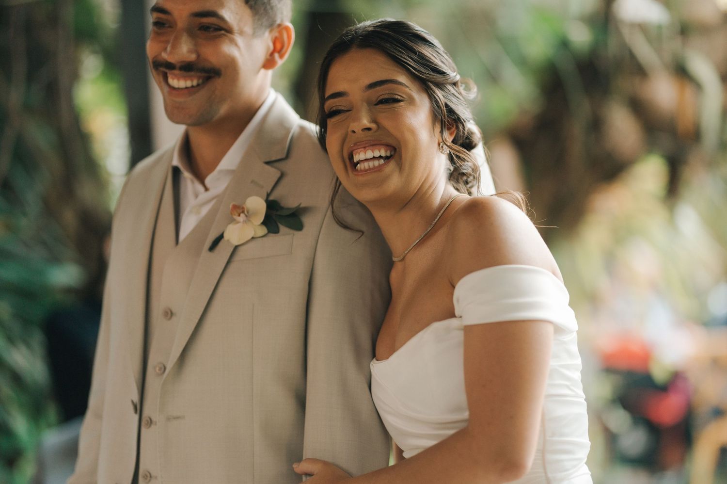 Happy newlyweds laughing together at outdoor wedding venue.
