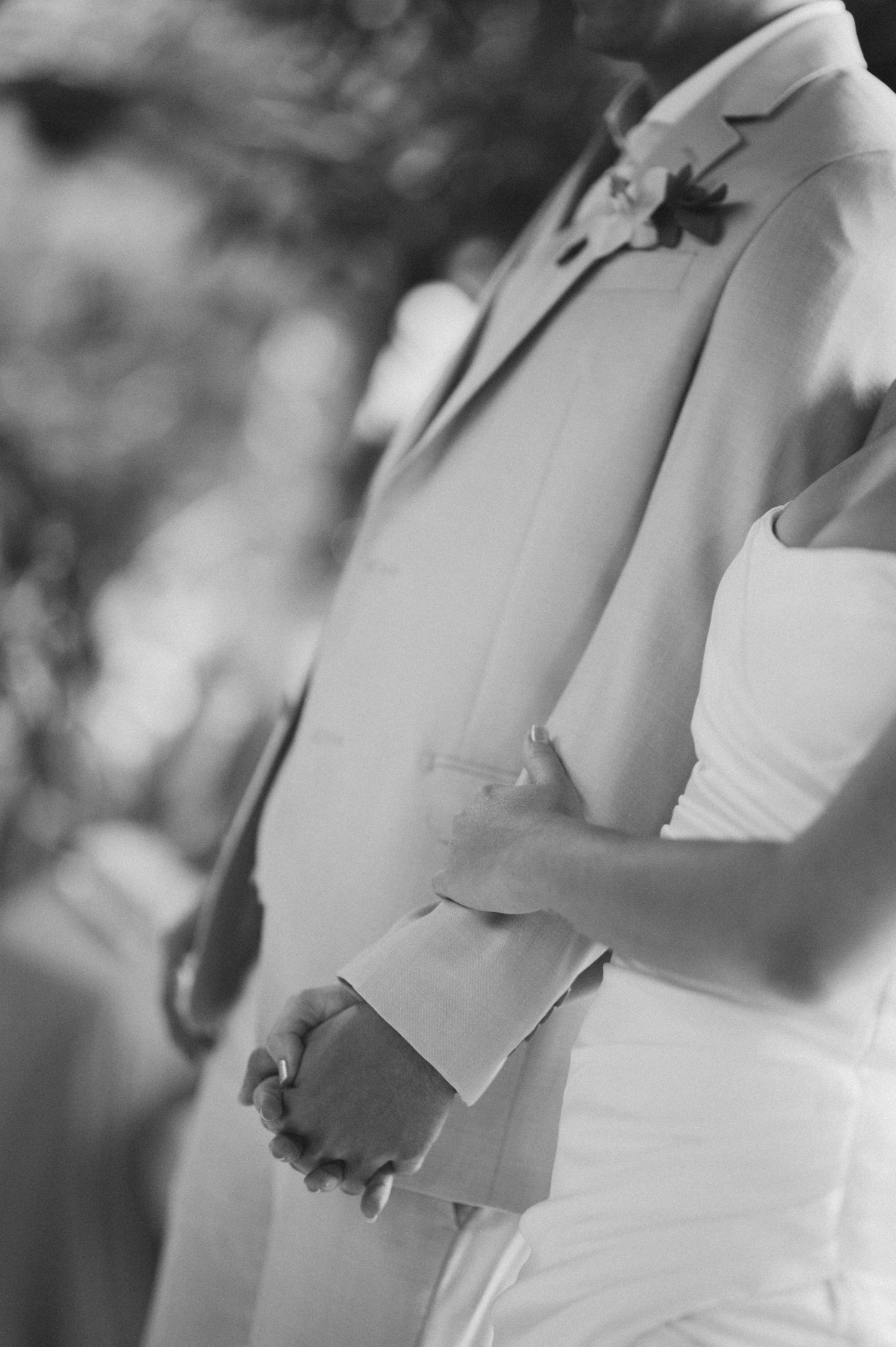 Black and white detail shot of couple holding hands during wedding ceremony.