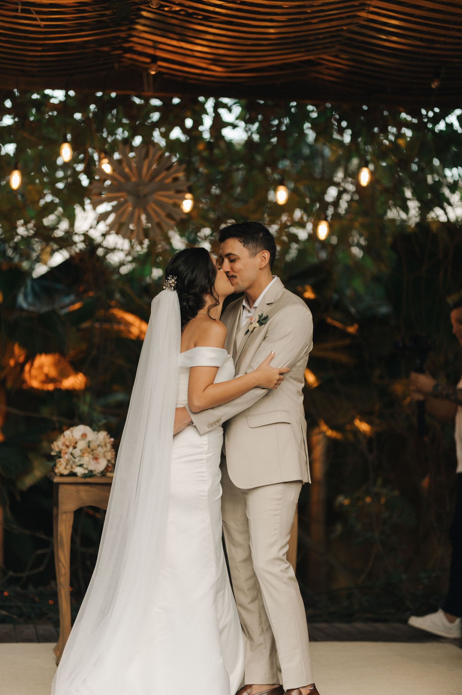 Intimate moment between newlyweds during their wedding ceremony under decorative lighting.