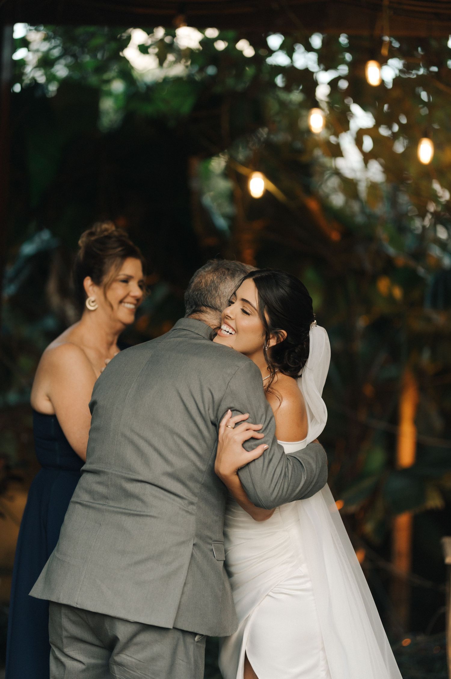 Emotional embrace during a wedding ceremony under string lights and foliage.