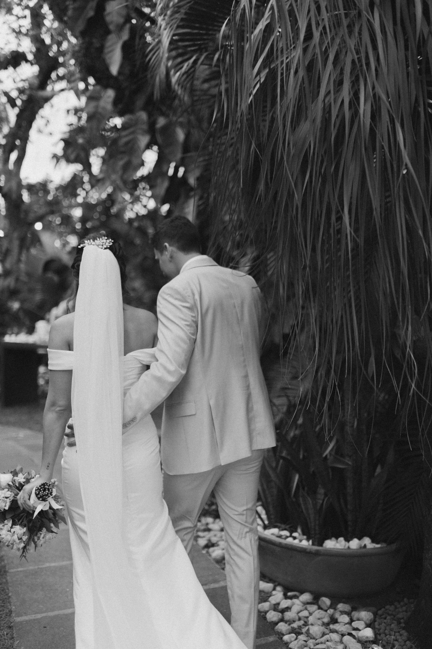 Black and white photo of a couple in wedding attire standing near palm trees.