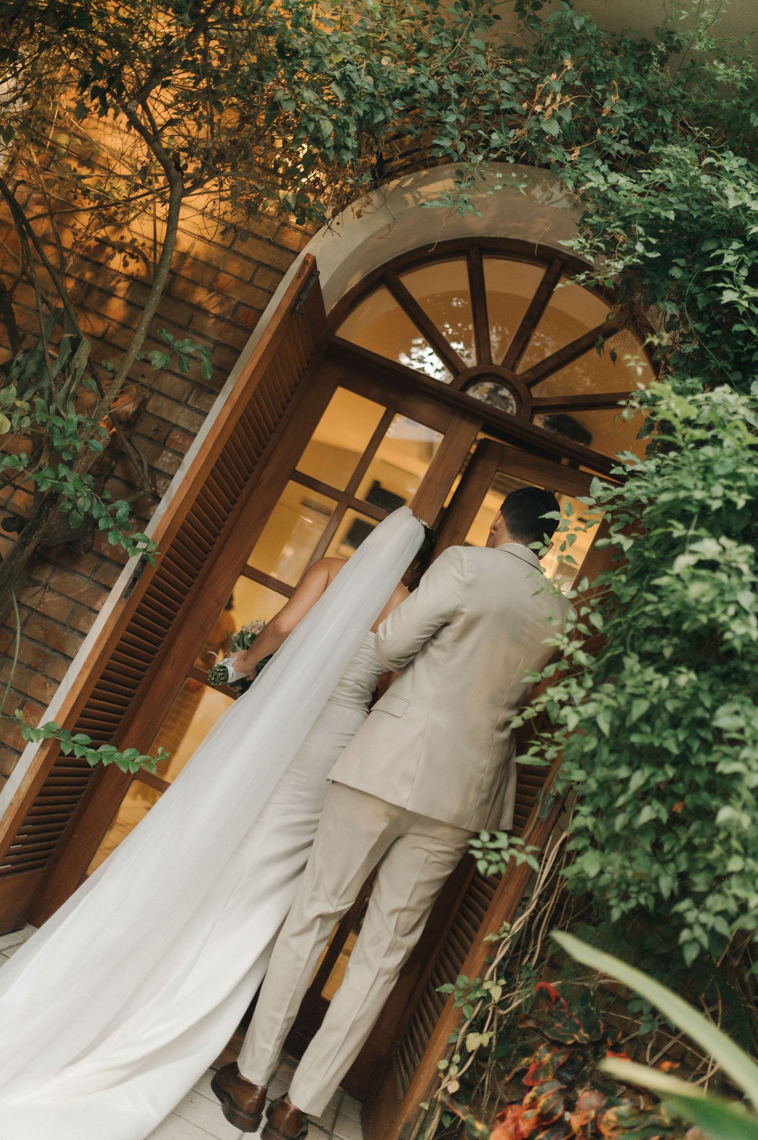 A romantic wedding photo showing a couple standing in front of an illuminated doorway framed by foliage.