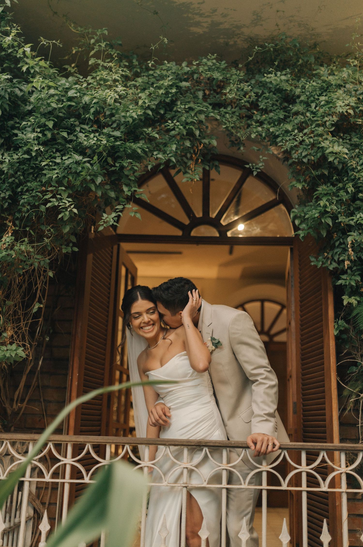 A tender wedding moment captured in front of an arched doorway with climbing vines.