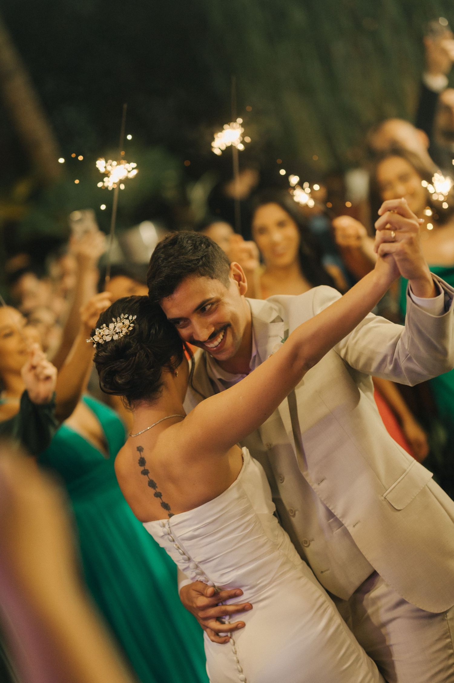 Joyful newlyweds dance together surrounded by sparklers and guests in green dresses.