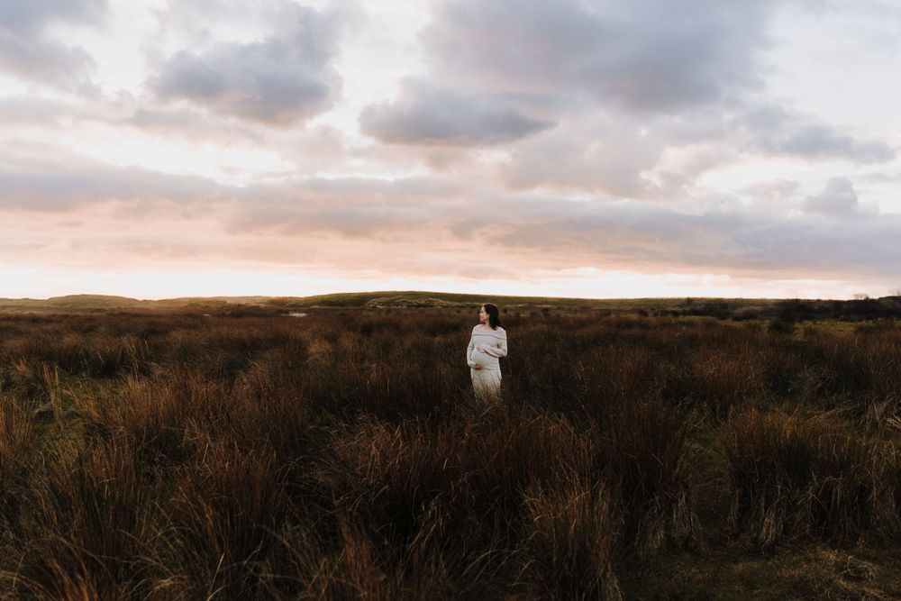 zwangere vrouw midden op een veld in de polder tijdens zonsondergang