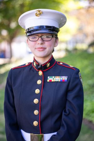 Marine in dress blues uniform with medals and cap standing at attention outdoors.
