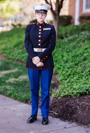 Marine dress uniform with white cap and brass buttons stands at attention on grassy slope.