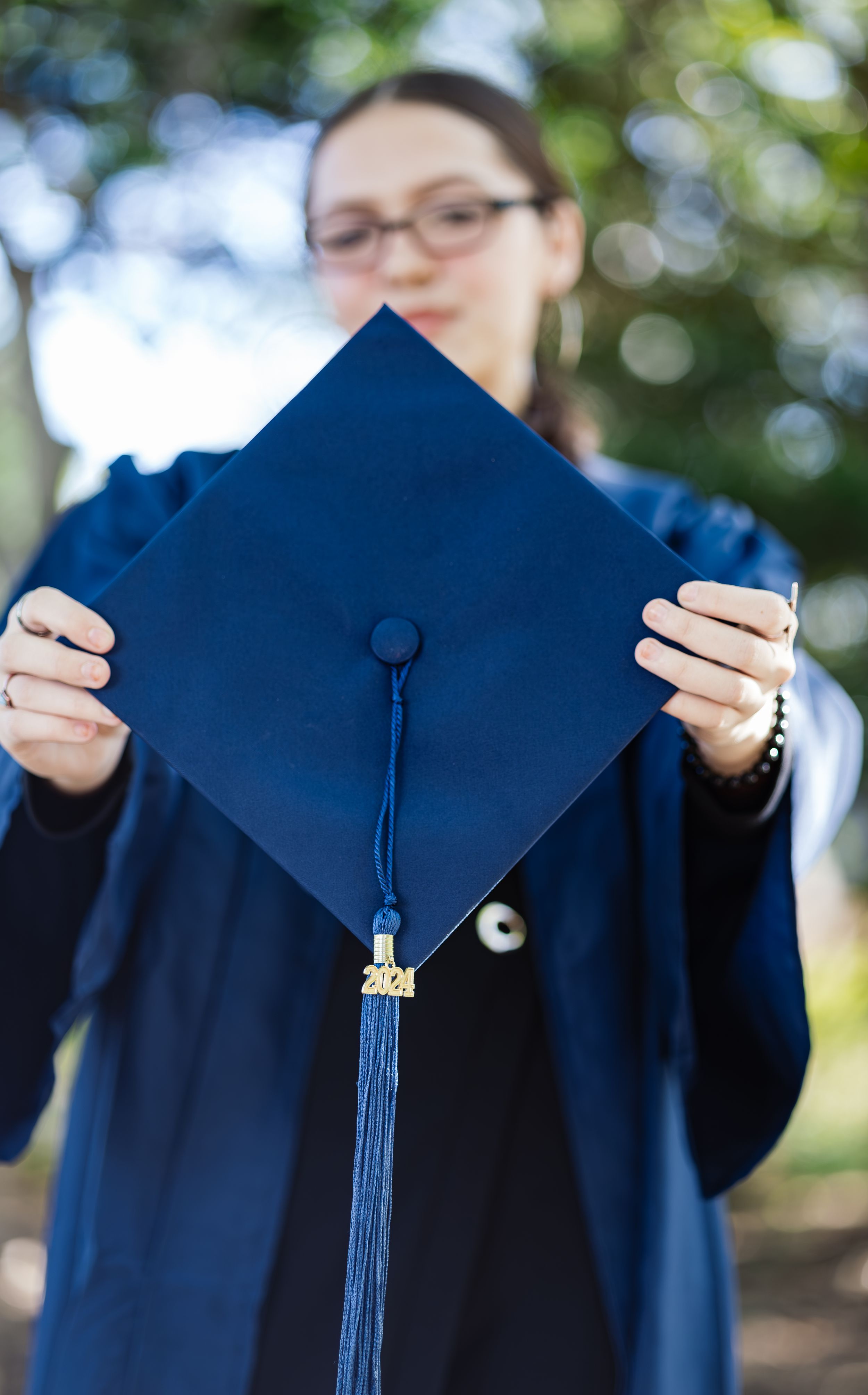 Graduate holding up blue graduation cap with tassel against blurred background.