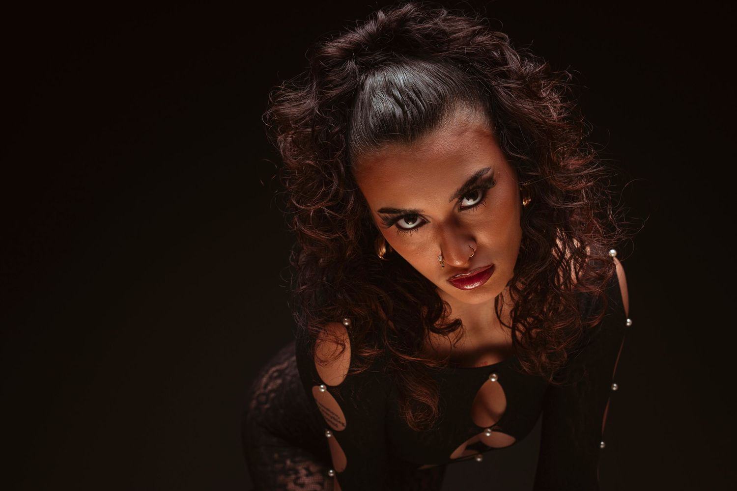 Dramatic low-key portrait with dark curly hair and moody lighting against black background.