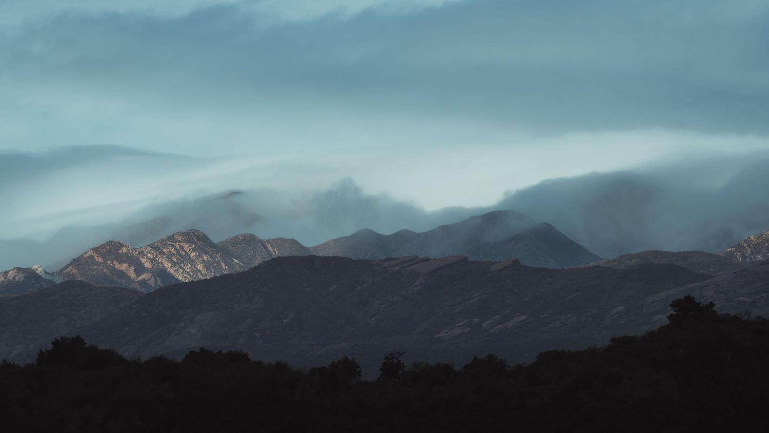 Panoramic winter landscape showing snow-covered mountains and terrain under dramatic cloudy skies.