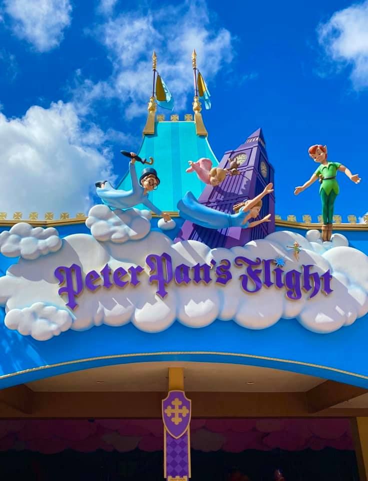 Peter Pan's Flight outdoor signage at Disney theme park with whimsical clouds and magical design elements against blue sky.