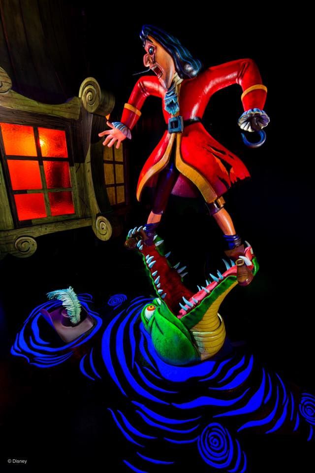 Colorful theme park animatronic display of a figure in red coat balancing on a crocodile above swirling blue water at night.