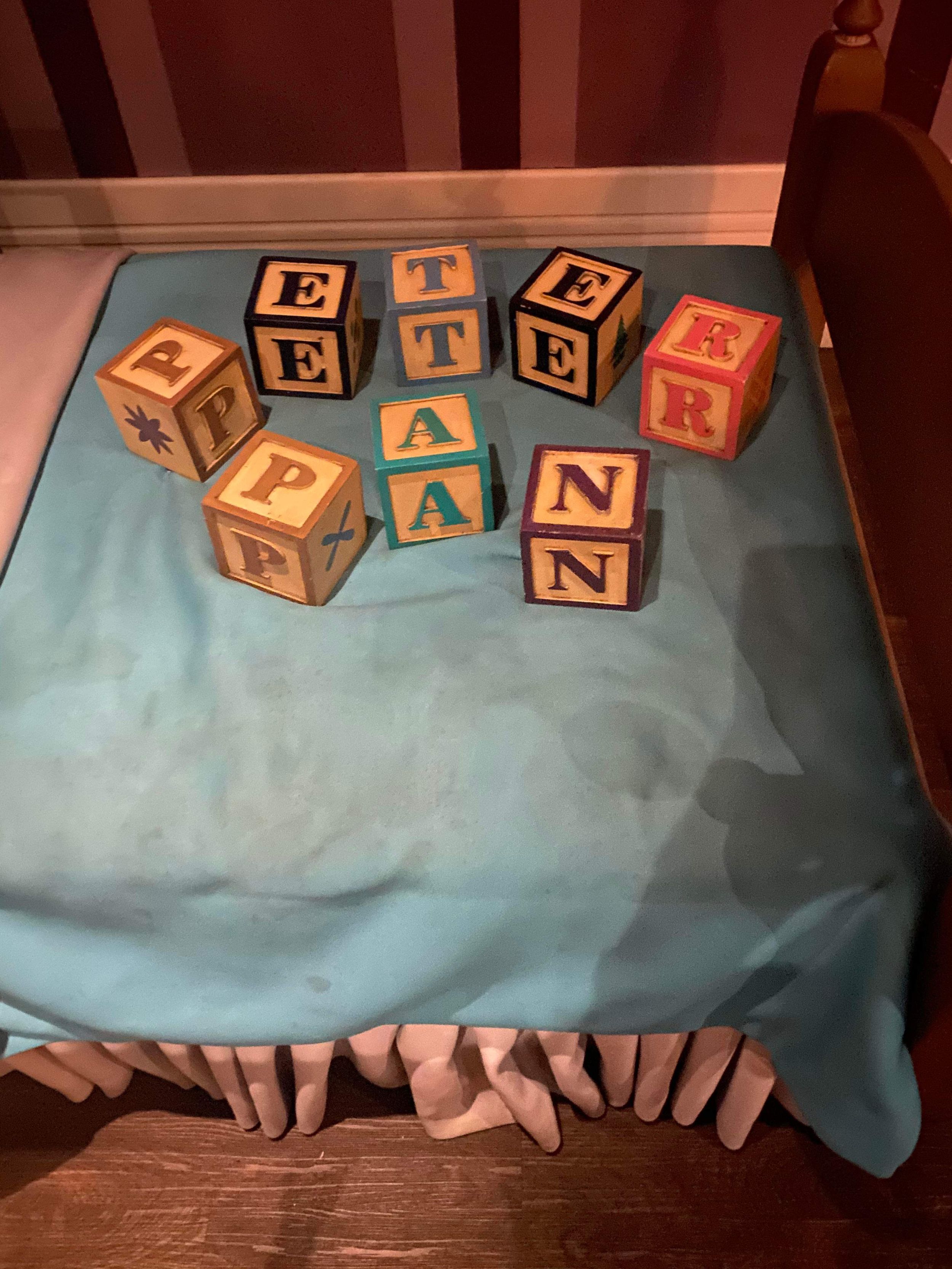 Wooden alphabet blocks on a turquoise tablecloth spell out letters in a scattered arrangement.