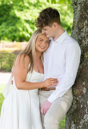 Couple in white outfits sharing intimate moments against a tree in a sunlit park.
