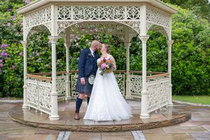 An ornate white garden gazebo provides an elegant backdrop for wedding photos on a stone patio.